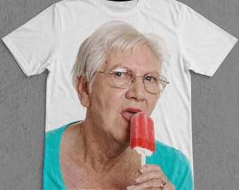 Pode incluir: T-shirt branco com uma imagem de uma pessoa mais velha com óculos a lamber um gelado vermelho. A pessoa está a usar um top turquesa. Um artigo de novidade para uso casual.