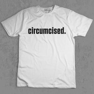 May include: White t-shirt with the word "circumcised." printed in black, centered on the chest. The shirt has short sleeves and a crew neck. The background is a plain, neutral grey.