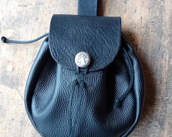 May include: A black leather pouch with a drawstring closure and a metal button. The pouch has a flap with a decorative metal button featuring a deer design.