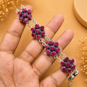 Pode incluir: Uma pulseira de prata com quatro motivos em forma de flor, cada um cravejado com seis pedras preciosas de rubi redondas de cor rosa profundo. Os motivos florais são ligados por elos duplos de prata, criando um design de corrente contínua.