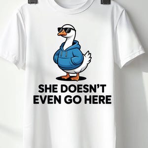 Pode incluir: Camiseta branca com um desenho de ganso de desenho animado usando óculos de sol e um moletom azul. O ganso está em pé com os braços cruzados. O texto "SHE DOESN'T EVEN GO HERE" está impresso em preto abaixo.