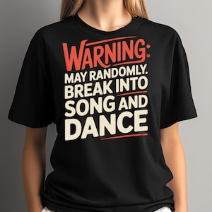 Op de afbeelding: Zwart T-shirt met de tekst "WARNING: MAY RANDOMLY BREAK INTO SONG AND DANCE" in rode en gebroken witte letters. Het shirt heeft een ronde hals.