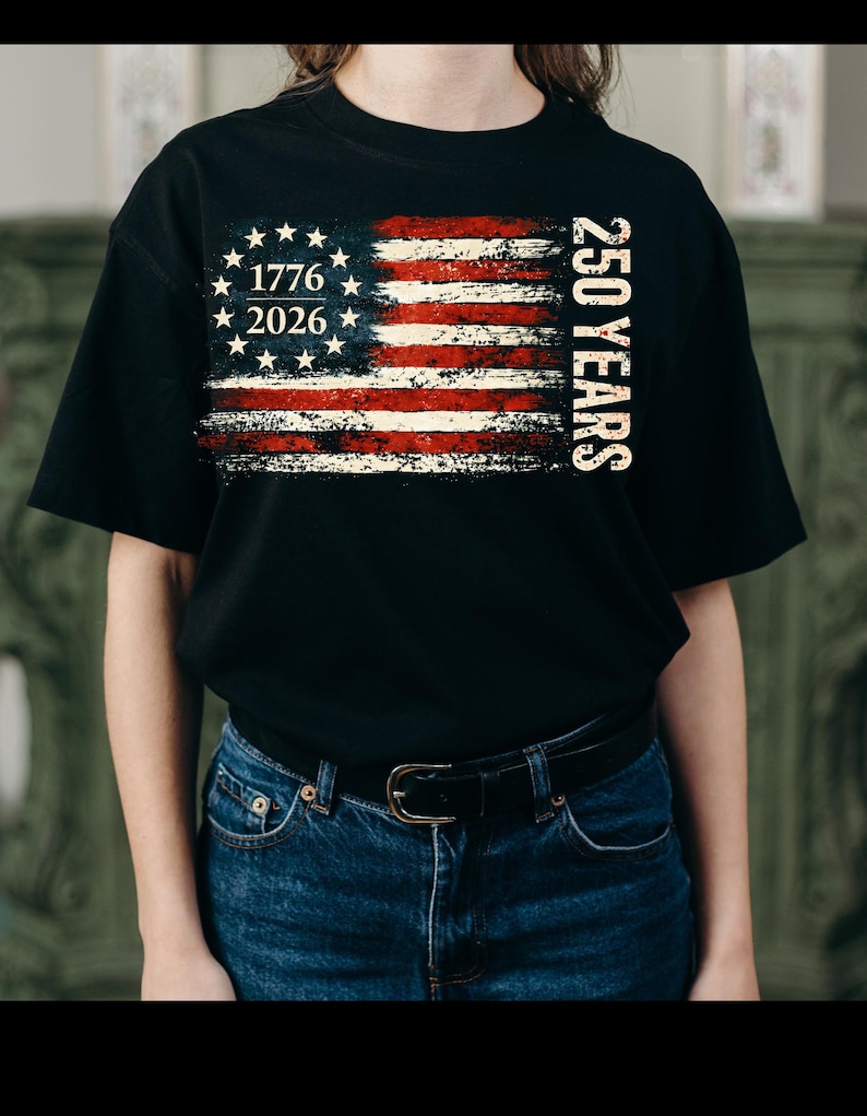Puede incluir: Camiseta negra con un dise&ntilde;o desgastado de la bandera estadounidense. El dise&ntilde;o incluye el texto "1776 2026" y "250 YEARS" en blanco. El dise&ntilde;o de la bandera presenta rayas rojas y blancas y un c&iacute;rculo de estrellas.