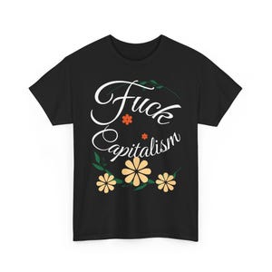 Op de afbeelding: Zwart T-shirt met de tekst "Fuck Capitalism" in witte letters, versierd met oranje en gele bloemmotieven. Het T-shirt heeft een ronde hals.