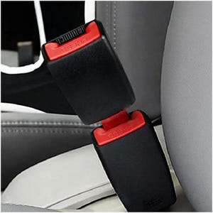May include: Close-up of two black car seat belt buckles with red release buttons. The word "PRESS" is visible on the red buttons. The buckles are connected and set against a grey car seat.