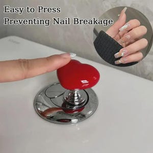 May include: A red heart-shaped toilet flush button with a chrome-finished circular base. The text "Easy to Press Preventing Nail Breakage" is displayed above the button, which is shown being pressed by a finger to demonstrate its function.