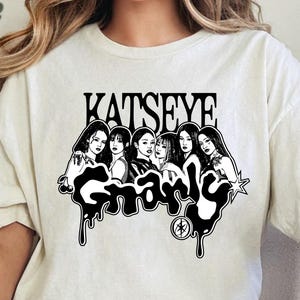 以下が含まれることがあります： クリーム色のTシャツ。6人の女性の白黒グラフィックと、上に「KATSEYE」、下に「Gnarly」の文字が描かれています。デザインは滴るような効果があります。シャツは柔らかい素材で作られています。