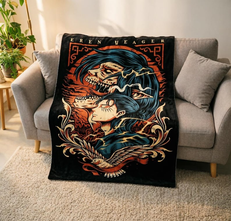 May include: A black rectangular throw blanket featuring a graphic illustration of Eren Yeager with a titan form above, orange and blue color accents, and a bird at the bottom. The text EREN YEAGER is printed in a stylized font at the top of the design.