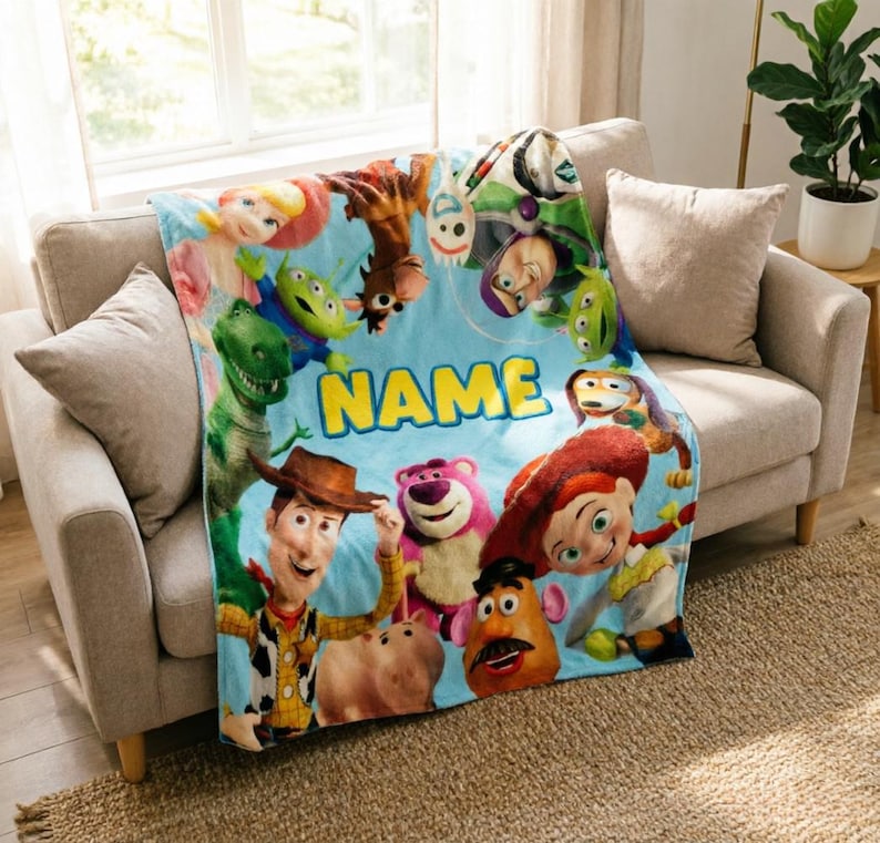 May include: A light blue fleece blanket featuring a colorful collage of Toy Story characters including Woody, Buzz Lightyear, Jessie, Rex, and Lotso. The word NAME is printed in large yellow block letters in the center of the blanket design.