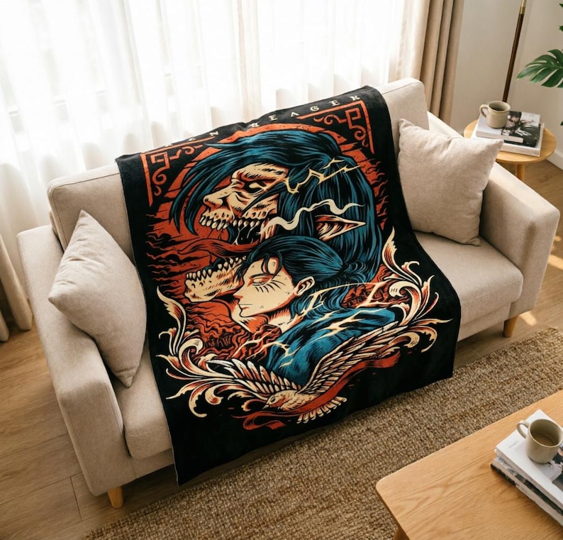 May include: A black throw blanket featuring a graphic illustration of a character with dark hair and a skeletal titan figure above them. The design includes orange and blue accents, intricate swirling patterns, and the text EREN YEAGER at the top.