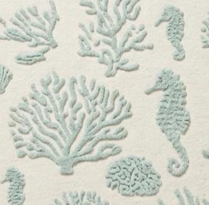 Puede incluir: Una tela textil con un patr&oacute;n repetitivo de caballitos de mar, ramas de coral y formas de coral cerebro bordadas en verde espuma de mar claro sobre un fondo blanco roto s&oacute;lido con un acabado de superficie suave y texturizado.