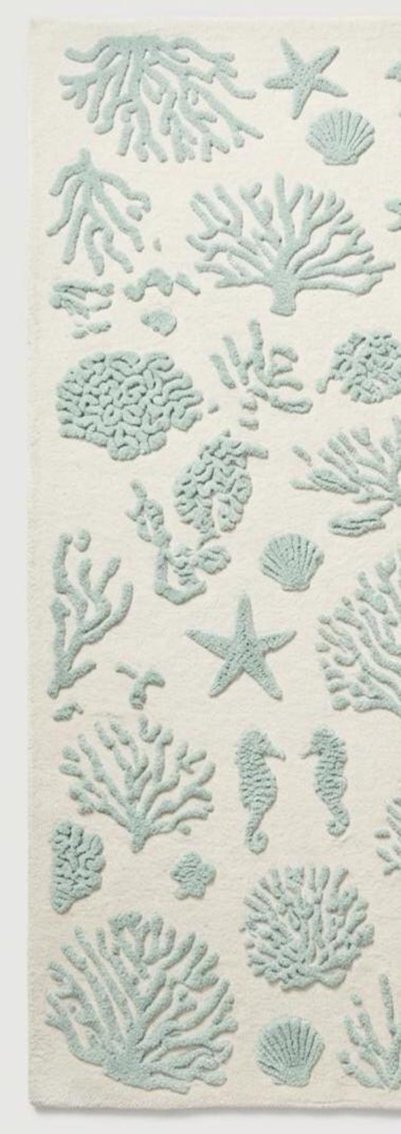 Puede incluir: Una alfombra rectangular con fondo color crema y un patr&oacute;n repetitivo de dise&ntilde;os en relieve de color azul claro. Los motivos incluyen varios tipos de corales, estrellas de mar, conchas marinas y caballitos de mar.