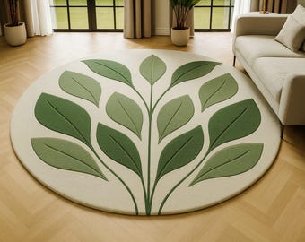 May include: A round rug with a cream-colored background and a large green leaf design. The leaves are various shades of green, creating a textured, three-dimensional effect. The rug is placed on a wooden floor in a well-lit room.