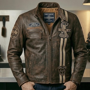 May include: A brown distressed leather jacket featuring a Ford Racing logo, a Shelby Cobra emblem, and a vertical racing stripe. The jacket includes a stand-up collar, a full-length front zip, and a Ford & Shelby Performance interior label.