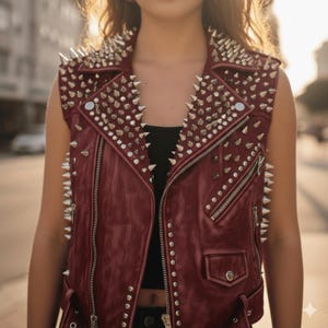 May include: A burgundy sleeveless leather vest with silver metal cone studs. The vest has a notched collar, a zip closure, and a small pocket. The vest is a bold fashion statement.
