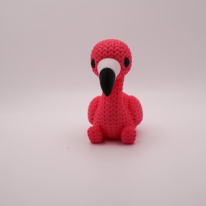 May include: A handcrafted, pink flamingo figurine with a textured surface. The flamingo has a black beak, white accents around the eyes, and is sitting upright. The figurine is a decorative item.