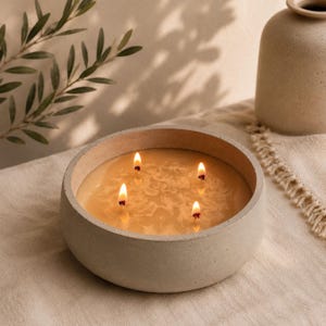 May include: A round, light beige concrete bowl candle featuring four lit wicks. The wax is a warm, golden yellow hue with a visible floral pattern embedded within the surface. The container has a smooth, matte texture and a thick, sturdy rim.