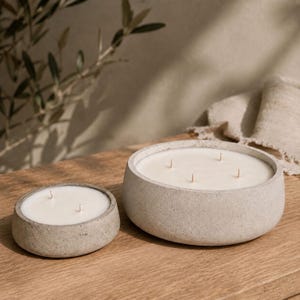 Peut inclure: Deux bougies rondes dans des contenants en béton gris clair avec de la cire blanche lisse. Le plus petit récipient possède deux mèches, tandis que le plus grand et plus large en contient quatre. Les deux ont une finition texturée.