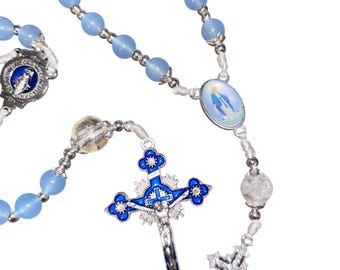 May include: A rosary with light blue beads and silver-toned metal accents. The cross is blue and silver, with a detailed depiction of Jesus. The rosary also features an oval pendant with a religious image.