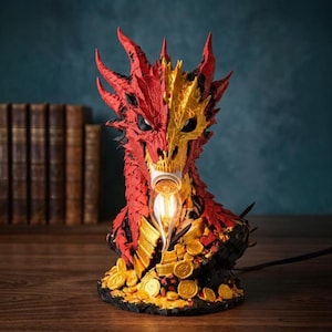 Könnte beinhalten: Eine drachenförmige Tischlampe mit einem geteilten rot-goldenen Kopf und komplexen Schuppentexturen. Der Drache sitzt auf einem Haufen Goldmünzen, wobei eine leuchtende Glühbirne in seinem Maul platziert ist. Der Sockel ist schwarz und strukturiert.