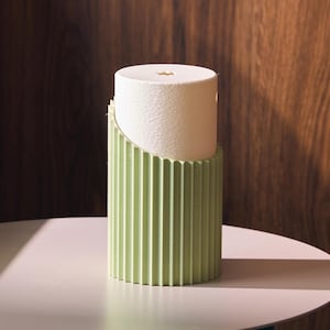 Peut inclure: Un rouleau de papier essuie-tout blanc est placé dans un support vert clair à rainures. Le support est cylindrique et présente des rainures verticales. L'arrière-plan est un grain de bois foncé.