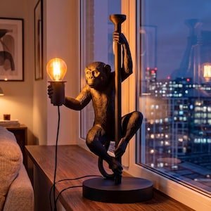 Pu&ograve; includere: Lampada da tavolo decorativa a forma di scimmia nera. La figura della scimmia tiene in mano una lampadina e si aggrappa a un palo. La lampada poggia su una base rotonda ed emette una luce calda. La lampada &egrave; alta circa 50 cm.