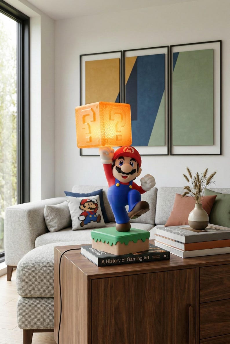 May include: A Mario-themed lamp featuring the character holding a glowing orange question mark block. The lamp is on a green and brown base, with a book titled "A History of Gaming Art" nearby. The lamp is a decorative item.