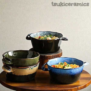 Peut inclure: Plusieurs bols en céramique de couleurs verte, bleue et noire, avec un glaçage unique et deux poignées. Les bols sont remplis de nourriture colorée. Le texte "tsukiceramics" est visible.