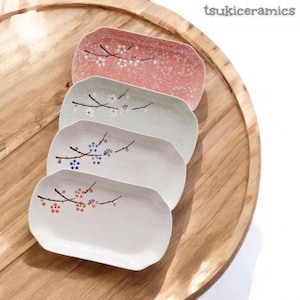 Könnte beinhalten: Vier rechteckige Keramik-Servierplatten mit floralen Zweigmustern in Rosa, Grün, Weiß und Off-White. Die Teller sind auf einem Holztablett angeordnet. Der Text "tsukiceramics" befindet sich in der oberen rechten Ecke.