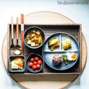 Può includere: Un vassoio di legno presenta un pasto completo con vari piatti. Il pasto comprende un piatto diviso con mais, zucca e altri elementi, più piccole ciotole di zuppa, pomodori e altri contorni. Sono incluse bacchette e posate.