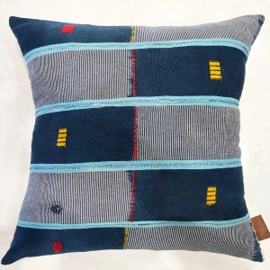 May include: A blue and white striped throw pillow with yellow and red accents. The pillow has a geometric pattern and is made of a woven fabric.