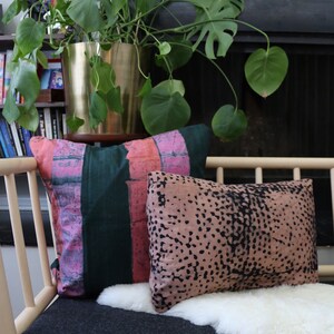 May include: A light wood bench with a black and gray cushion and a white sheepskin throw. Two pillows are on the bench, one with pink and green stripes and the other with a brown and black speckled pattern.