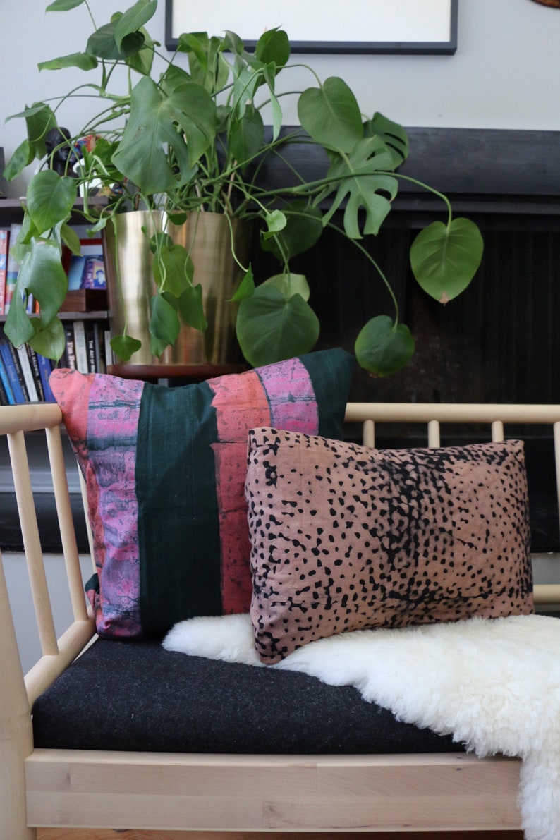 May include: A light wood bench with a black and gray cushion and a white sheepskin throw. Two pillows are on the bench, one with pink and green stripes and the other with a brown and black speckled pattern.