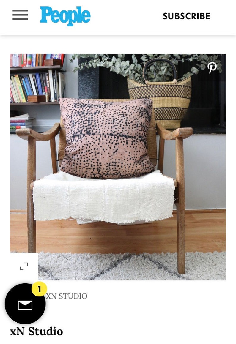 May include: A wooden chair with a white throw blanket and a pink and black patterned pillow. The chair is in front of a bookshelf and a basket.