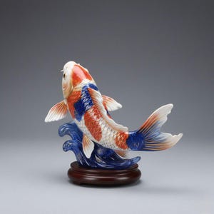 May include: A ceramic koi carp sculpture in red, white, and blue. The fish is depicted swimming, above a blue wave design, and set on a dark wooden base. The sculpture is a decorative item, suitable for display.