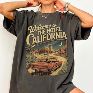 May include: Dark gray t-shirt with a graphic that reads "Welcome to The Hotel California." The graphic features a red convertible car driving on a desert road towards a hotel, with cacti and mountains in the background.