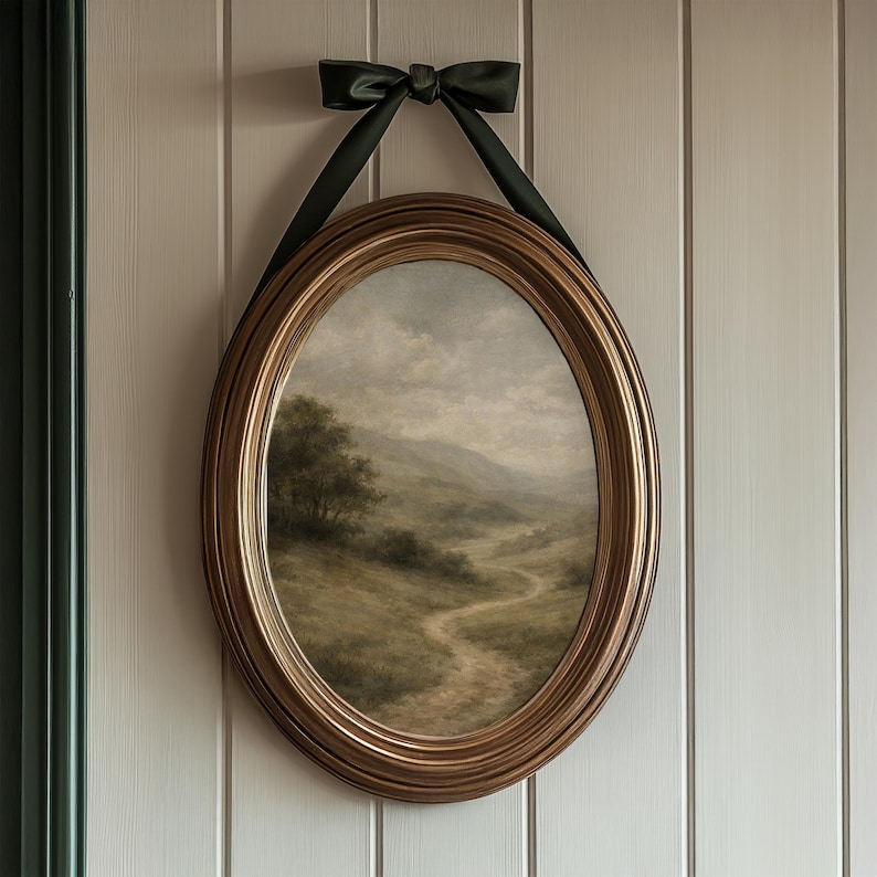 Pode incluir: Pintura de paisagem oval emoldurada em ouro. A obra retrata um caminho sinuoso atrav&eacute;s de uma colina gramada, com &aacute;rvores e montanhas ao fundo. Uma fita verde escura &eacute; amarrada no topo para pendurar.