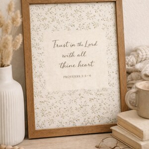 Puede incluir: Una impresi&oacute;n enmarcada con el texto "Conf&iacute;a en el Se&ntilde;or con todo tu coraz&oacute;n" y Proverbios 3:5-6. La impresi&oacute;n tiene un patr&oacute;n floral y est&aacute; en un marco de madera. Tambi&eacute;n se ven un jarr&oacute;n blanco, libros y una taza.