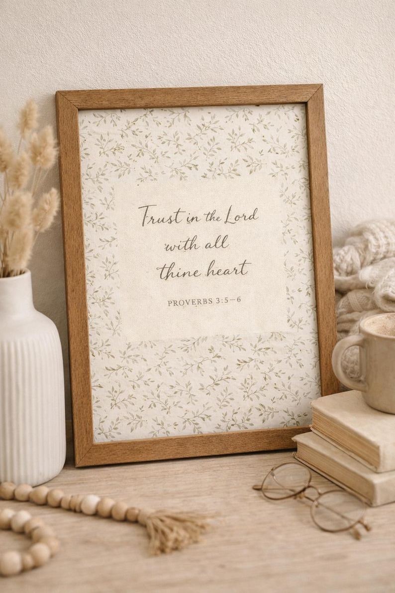 Puede incluir: Una impresi&oacute;n enmarcada con el texto "Conf&iacute;a en el Se&ntilde;or con todo tu coraz&oacute;n" y Proverbios 3:5-6. La impresi&oacute;n tiene un patr&oacute;n floral y est&aacute; en un marco de madera. Tambi&eacute;n se ven un jarr&oacute;n blanco, libros y una taza.
