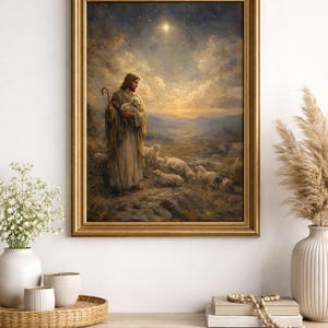 May include: A framed print depicts a religious scene with a figure holding a lamb, surrounded by sheep. The artwork is set against a backdrop of a starry sky and rolling hills, framed in a gold-colored ornate frame. The print is displayed on a white cabinet.