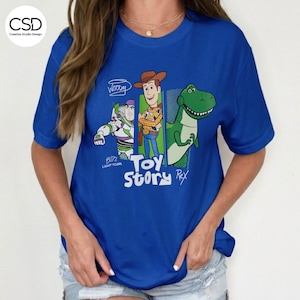 Puede incluir: Una camiseta azul real con personajes de la pel&iacute;cula de animaci&oacute;n "Toy Story". El dise&ntilde;o incluye a Woody, Buzz Lightyear y Rex, con las palabras "Toy Story" en una fuente l&uacute;dica. La camiseta tiene mangas cortas.