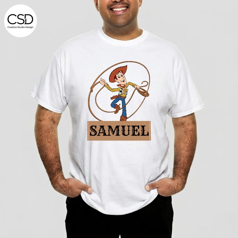 Puede incluir: Camiseta blanca con una imagen de dibujos animados de Woody de Toy Story, sosteniendo un lazo. El nombre "SAMUEL" est&aacute; impreso en una pancarta rectangular marr&oacute;n debajo. La camiseta es de cuello redondo.