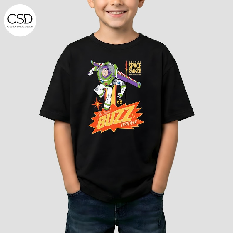 May include: Black t-shirt featuring a graphic of Buzz Lightyear in a dynamic pose, with the text "The Original Buzz Lightyear" and "Deluxe Space Ranger Action Figure". The design is in vibrant colors, including green, purple, and orange.