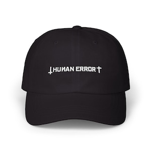 May include: Black baseball cap with the text "HUMAN ERROR" in white, featuring a cross and a reversed cross. The cap has a curved brim and a classic six-panel design.