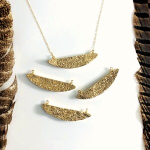 May include: Four gold-toned crescent-shaped pendants with a sparkly glitter finish. The pendants are strung on a gold chain.