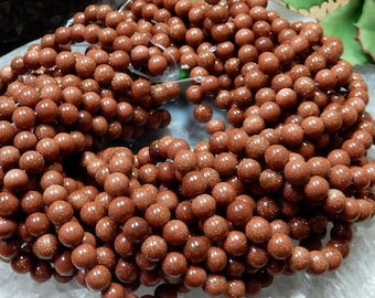 May include: A strand of brown sandstone beads, each bead is round and has a slightly textured surface.