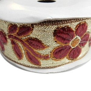 May include: Gold and burgundy trim with a floral design. The trim is rolled up on a white spool.