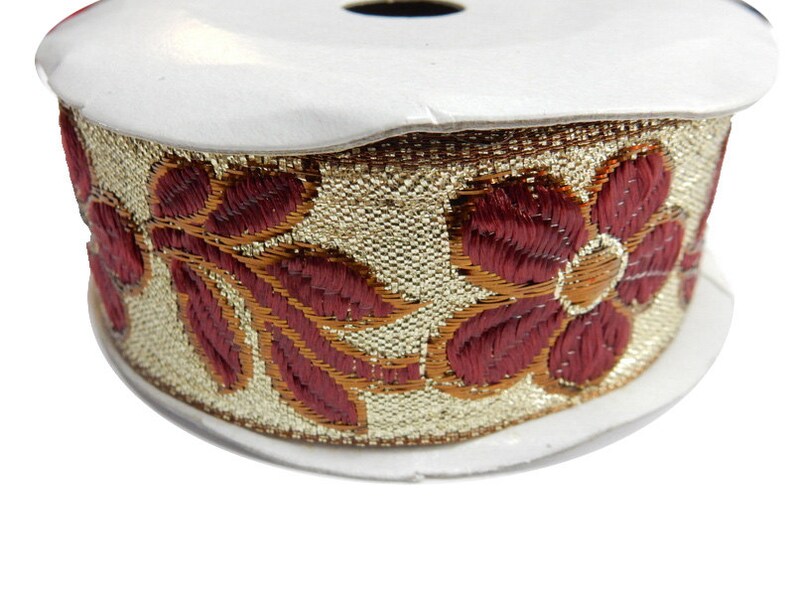 May include: Gold and burgundy trim with a floral design. The trim is rolled up on a white spool.