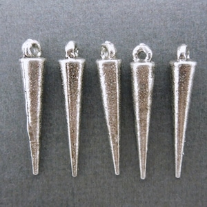 Puede incluir: Cinco colgantes de metal de color plateado en forma de conos puntiagudos. Los colgantes tienen un bucle en la parte superior para sujetarlos a un collar o pulsera.