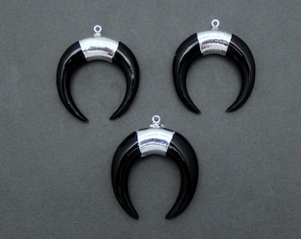 Peut inclure: Trois pendentifs en forme de croissant de lune noirs avec des accents métalliques argentés. Chaque pendentif a une petite boucle en haut pour l'attacher à une chaîne ou à un autre composant de bijou. Les pendentifs sont présentés sur un fond gris.